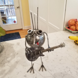 A small metal sculpture of a cute creature playing a Les Paul guitar